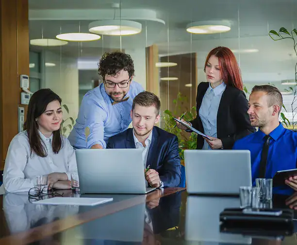 Teamarbeit im Büro mit fünf Personen, die an Laptops arbeiten.